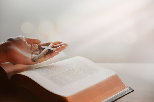 하나님의 생명의 말씀 성경책 위로 예수 그리스도의 십자가를 들고 있는 신자의 손, 신앙적 묵상의 시간 배경
