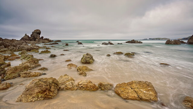 Las Meninas rocks on the westernmost end of Playa de Penarronda Beach, at rising tide in a cloudy yet colorful springtime sunset. Asturias-Spain-002