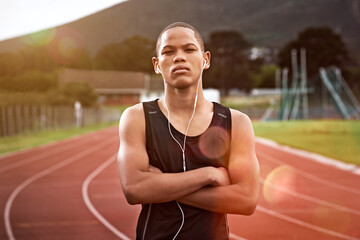 Naklejka premium Fitness, portrait and teenager in stadium with earphones, music and crossed arms for sports event. Athlete, runner and African person with audio, track and serious for exercise, training and practice