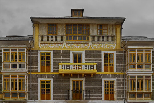 Facade of 'cube' style Indiano house of plastered walls painted gray with white bands, yellow decoration, and side oriels. Luarca-Asturias-Spain-022