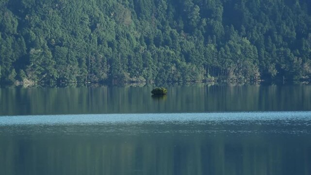 Lone islet mirrored in the glassy surface of Lagoa das Sete Cidades, Sao Miguel, Azores, Portugal