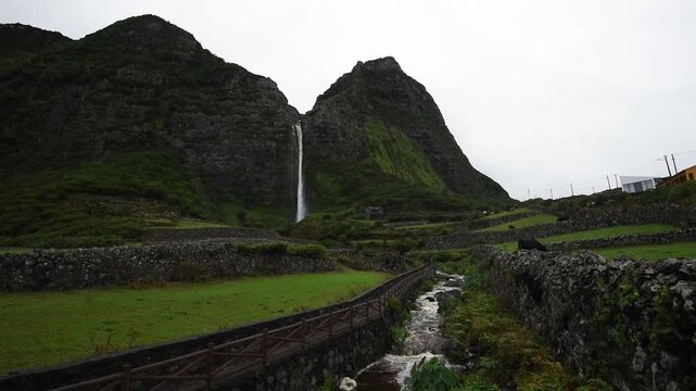 Poco do Bacalhau waterfall dropping between peaks above walled pastures, Faja Grande, Flores, Azores, Portugal