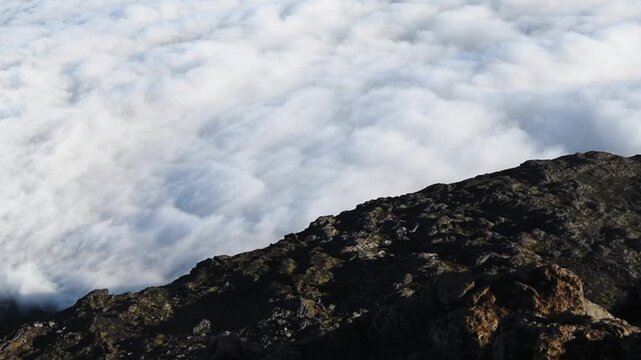 Volcanic scoria of the summit slope of Mount Pico falls away into a cloud deck, Pico, Azores, Portugal