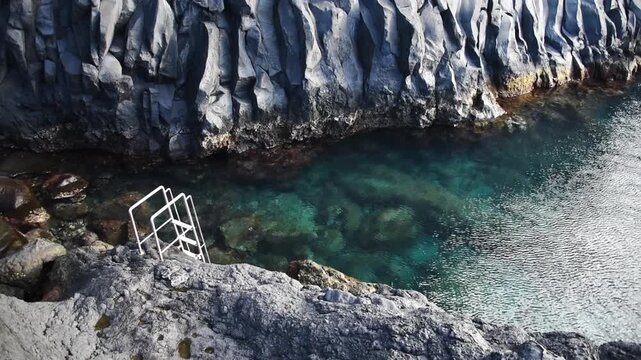 Piscina Natural "Simao Dias" Clear turquoise water and a bathing ladder in a natural rock pool beneath basalt, Sao Jorge, Azores, Portugal