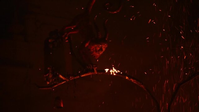 Horned falla figure silhouetted amid flying embers at the Crema, Las Fallas, Valencia, Spain, in fire-lit darkness.