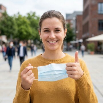 Smiling Woman Removes Face Mask Giving Thumbs Up Outdoors In City Street