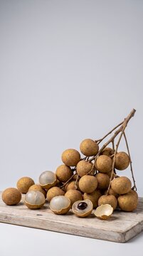 Fresh duku fruits whole and peeled on a wooden board, studio lighting