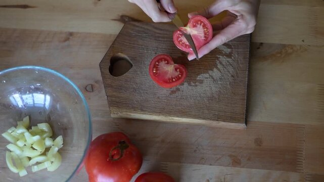 Woman's hands slicing fresh red tomatoes on wooden cutting board and putting them into glass bowl for vegetable salad