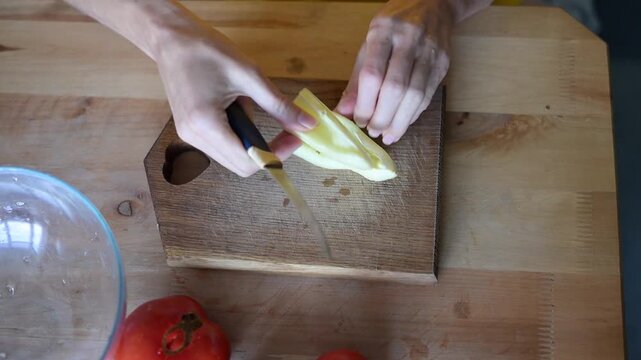 Woman's hands chopping sweet bell pepper on wooden cutting board for healthy salad meal preparation in kitchen