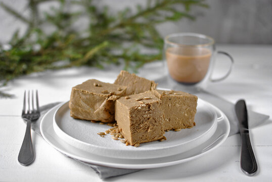 Sunflower seed halva slices served on a white plate with coffee and green branches in a bright festive setting.
