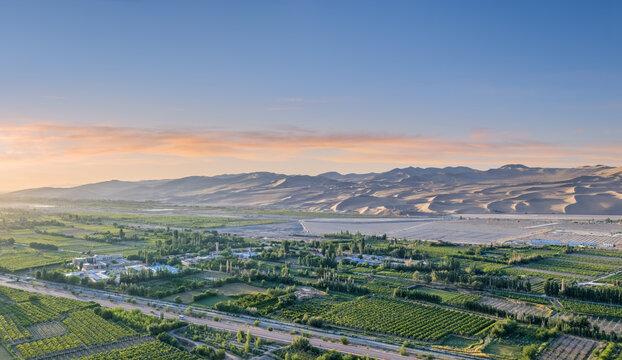 Aerial View of Lush Green Oasis and Vast Sand Dunes at Sunrise in Dunhuang
