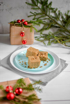 Sunflower halva cubes with seeds on a turquoise plate, surrounded by Christmas gifts, red ornaments and evergreen branches.