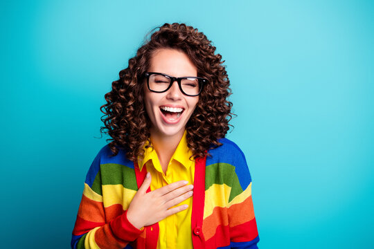 Joyful young woman laughing wearing glasses and a colorful rainbow cardigan against a bright teal background, cheerful portrait expressing happiness, confidence and playful style