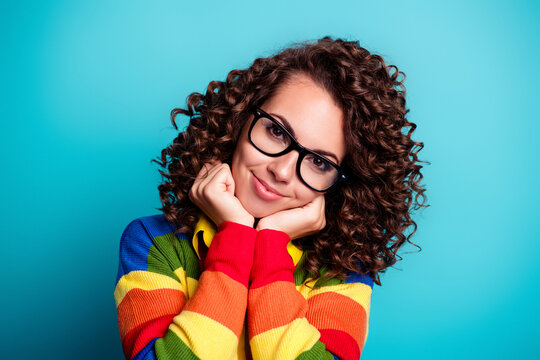 Portrait of a smiling woman with glasses and curly hair wearing a colorful sweater against a bright blue background