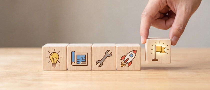 Hand placing a wooden block with a flag icon on a row of blocks representing the business development and project process