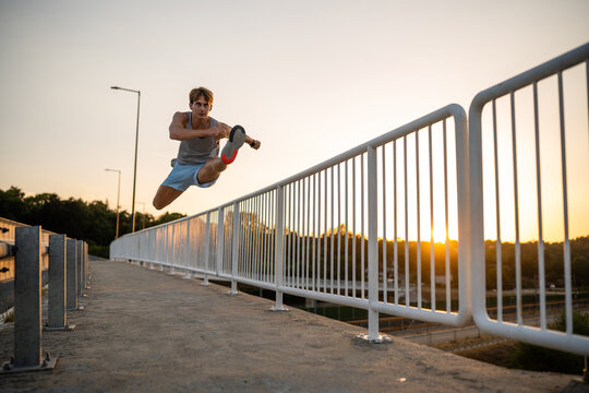 Man jumping over railing practicing parkour at sunset