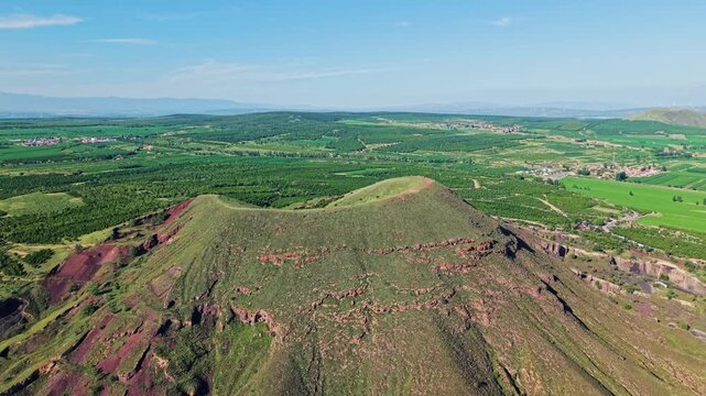 Aerial forward tilt down revealing dramatic sunlight and shadows on steep cinder cone volcano slopes and rugged geological terrain.