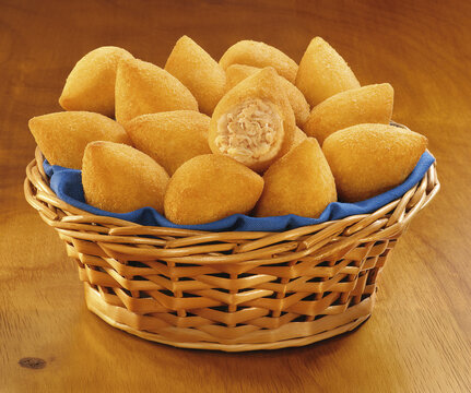 Cesta de vime com por&ccedil;&atilde;o de coxinhas de frango crocantes recheadas sobre mesa de madeira