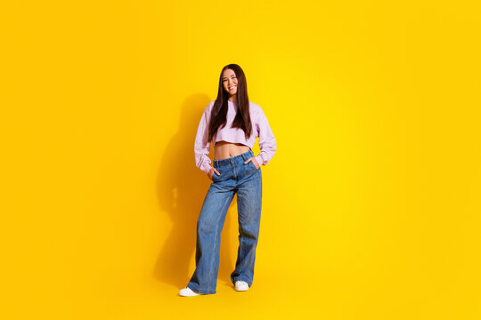 Smiling young woman in casual fashion crop top and wide jeans standing confidently against vibrant yellow background
