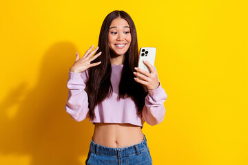 Plakat Young woman excitedly looking at her smartphone during a surprised selfie and video call in a casual crop top and jeans against a bright yellow studio background