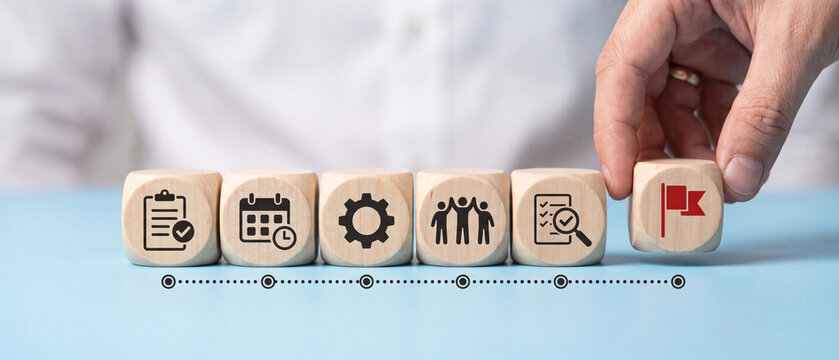 Hand placing a wooden block with a red flag icon, representing the final step in a business process or project completion