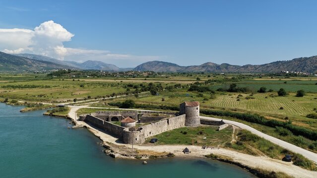Aerial view of the Venetian Castle of Butrint situated on the edge of the water, surrounded by green fields and mountains in Ksamil, Vlore County, Albania.