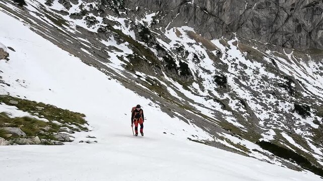 Solo male hiker on a dangerous mountain trail climbing up a large snowfield wearing crampons in Durmitor National Park in Montenegro