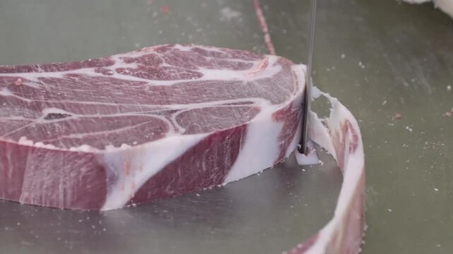 Ribeye steak sliced by knife in professional butcher station with gloved hands on stainless cutting surface, revealing marbling and bone edge under bright diffuse light on green worktable