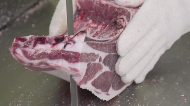 Rib meat slicing with gloved hands knife cutting surface closeup in butcher kitchen showing marbling fat bone edges texture hygienic stainless steel environment