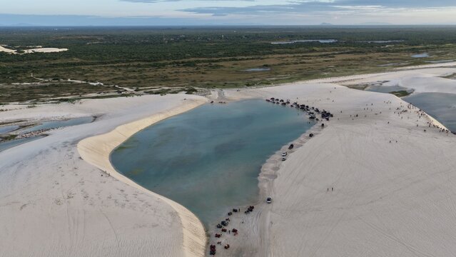 Aerial view of Parque Nacional dos Lencois Maranhenses featuring vast white sand dunes and crystal clear lagoons with off-road vehicles parked along the shore in Atins, Maranhao, Brazil.