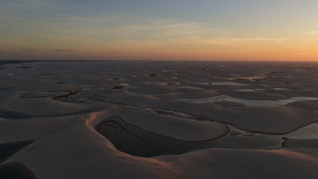 Aerial view of the vast white sand dunes and turquoise lagoons of Parque Nacional dos Lencois Maranhenses at sunset in Atins, Maranhao, Brazil.