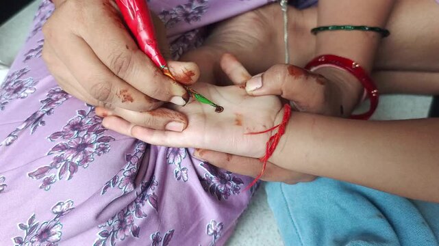 Woman applying traditional henna mehendi design on child palm during festival celebration close up