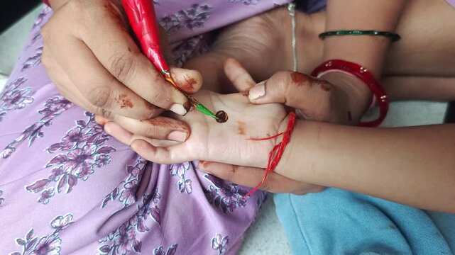 Woman applying traditional henna mehendi design on child palm during festival celebration close up