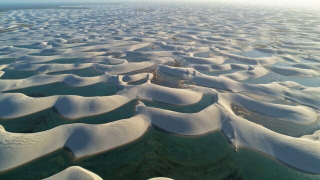 Aerial view of Parque Nacional dos Lencois Maranhenses featuring vast white sand dunes and crystal clear turquoise lagoons under soft sunlight in Atins, Maranhao, Brazil.