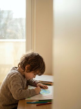 A young child drawing with colored pencils at a wooden table indoors. Expressing creativity through colorful artwork and imagination. World Children's Day concept.