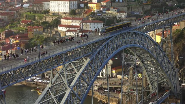 Aerial view of the iconic Dom Luis I Bridge in Porto, featuring a metro train crossing the upper deck with pedestrians, overlooking the Douro River in Porto, Porto District, Portugal.