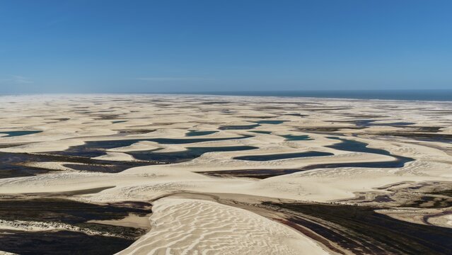 Aerial view of Parque Nacional dos Lencois Maranhenses with its vast white sand dunes and seasonal rainwater lagoons under a clear blue sky in Atins, Maranhao, Brazil.
