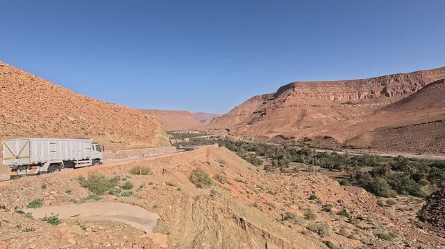 Canyon road winding past palm groves below red cliffs, Ziz Canyon, Errachidia, Draa-Tafilalet, Morocco
