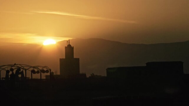 Scaffolded Ben Youssef Mosque minaret above the medina rooftops at dusk with a contrail, Marrakech, Morocco