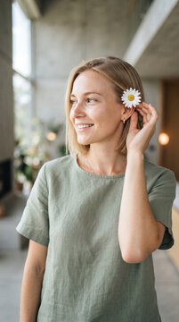 Smiling blonde woman tucking a daisy flower behind her ear indoors