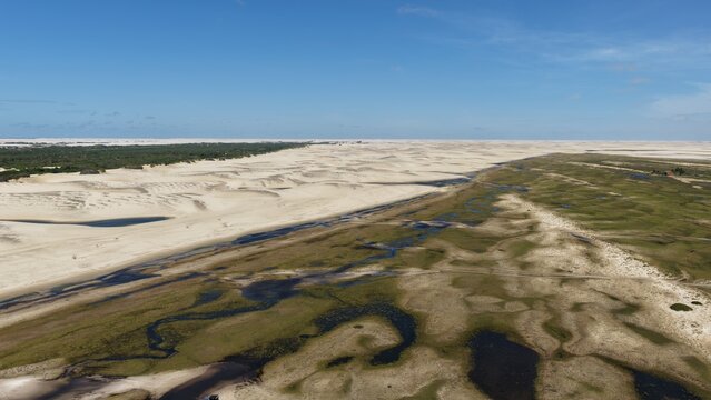 Aerial view of the vast white sand dunes and seasonal lagoons of Parque Nacional dos Lencois Maranhenses, with lush green vegetation and winding water channels in Atins, Maranhao, Brazil.