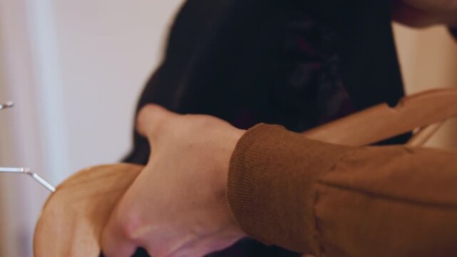 Close up of person hand holding and adjusting fabric on wooden hangers in indoor setting. focus remains consistently on interaction between hands clothing items and hanging mechanisms. Soft