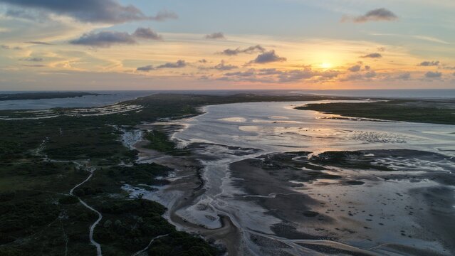Aerial view of Parque Nacional dos Lencois Maranhenses featuring vast sand dunes, winding waterways, and lush vegetation under a golden sunset sky in Atins, Maranhao, Brazil.