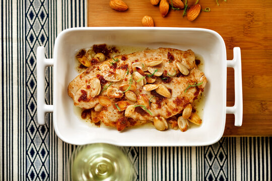 Roasted fish fillet with nuts and lemon zest in a white dish, viewed from above
