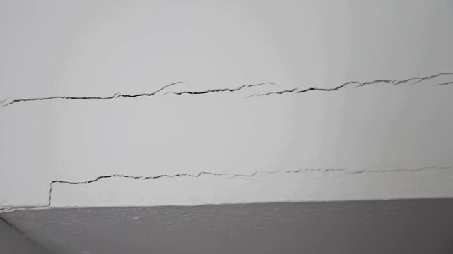 close up following cracks in white wall tilting up and panning right small crack home repaire home insurnace insurance damage construction.