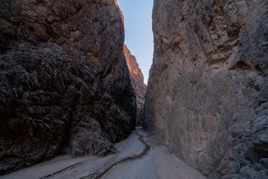 Wide shot of deep narrow rocky gorge with towering granite cliffs and winding gravel pathway in Tayyib Al Ism, Tabuk