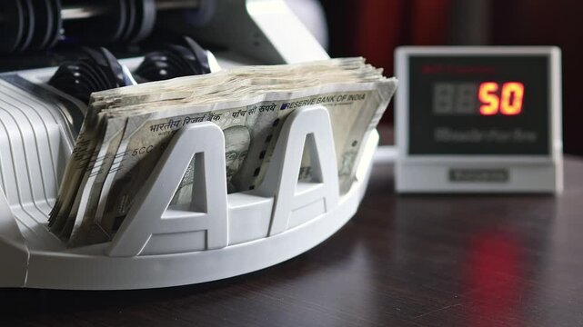 Indian Rupee Banknotes in Automatic Counting Machine. Paper bills move through a currency counter tray. Banking, accounting, cash handling, financial control and business operations concept.