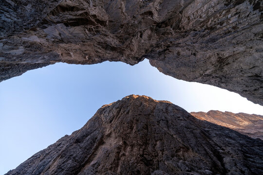 Low-angle perspective looking up at massive steep granite rock walls framing a clear blue sky in Tayyib Al Ism gorge, Tabuk