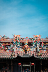 Fototapeta premium Porcelain sculptures of two dragons on the roof of a temple in Quanzhou contrast with the blue sky