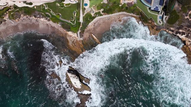 Aerial view of Crystal Cove with waves crashing against rocky cliffs and coastal landscape in Newport Beach, California, United States.